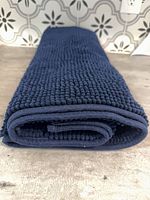 Rolled navy chenille bath mat showing edge binding