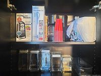 Overall view of boxed appliances, stack of red cups, bagged napkins, and glass canisters on shelf