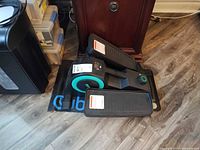 Elliptical on branded mat, side view showing pedals and teal flywheel