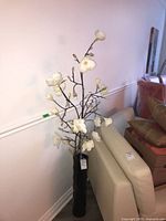 Full view of magnolia arrangement in tall black vase against wall