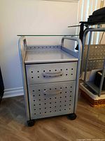 Front and side view showing two drawers, perforated panels, glass top shelf, caster wheels