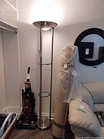 Full view of metal floor lamp illuminated, showing overall structure and shelves