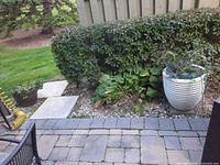 Large light grey ribbed planter placed on patio slab beside shrubs