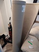 Rolled beige rug standing upright beside furniture