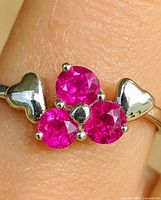 Front view of white gold ring showing three round rubies and heart shoulders