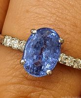 Close-up of ring on finger showing tanzanite and diamond shoulders