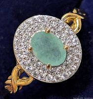 Front view of ring showing emerald-colored center stone and clear halo