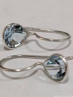 Two silver hook earrings with bezel-set pale blue stones, side view