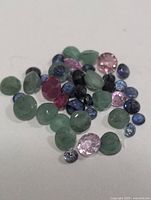 Pile of mixed green, pink and blue faceted gemstones on white background