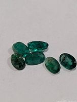 Six oval emerald gemstones on white surface