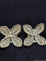 Front view of both silver-tone four-petal flower earrings on dark background