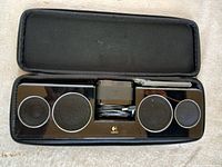 Speaker unit inside open carrying case showing four speaker grilles and accessories