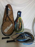 Group shot of Wilson tennis racket in cover, yellow Le Pro racquetball racket, two black/blue racquetball rackets