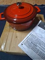 Closed Dutch oven on shipping box next to manual
