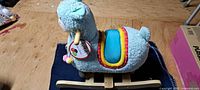 Side view of plush llama on wooden rocker base showing saddle and tag