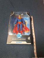 Front view of sealed DC Multiverse Superman figure box with ruler for scale
