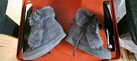 Pair of grey faux-fur wedge boots side view on red surface