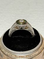 Ring front view showing central diamond, green sapphire halo, pavé diamonds, filigree work