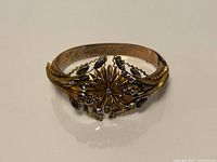 Front view of gold-tone floral bangle showing raised flower and leaves