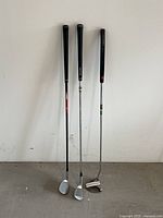 Full view of three golf clubs standing upright showing grips, shafts and heads