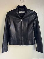Front view of black leather jacket on hanger showing zipper and collar