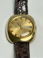 Front view of Birks automatic watch showing gold-tone dial, day/date window, gold-filled cushion case, leather strap