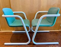 Side view of both Kinetics armchairs showing white tubular frames and teal upholstery