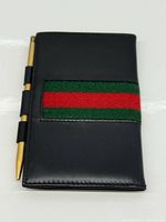 Front view of black leather address book with green-red web stripe and gold-tone pen
