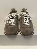 Front view of taupe suede sneakers with white laces on box