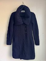 Full view of navy cable knit cardigan coat on hanger showing overall design, collar and buttons
