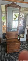 Full view of solid wood hall tree showing mirror, carved crest, coat hooks, armrests, and storage bench