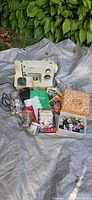 Overall view showing Singer sewing machine, cords, manuals, books, trays, jars, sewing box and assorted sewing notions