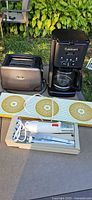 All four appliances arranged outdoors: toaster, coffee maker, warming tray, electric knife in tray