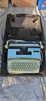 Typewriter in open carry case showing keyboard, platen, and power cord