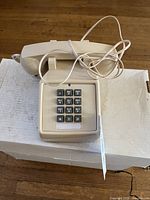 Front view of beige corded push-button telephone showing handset, keypad and cables