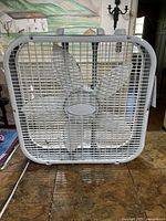 Front view of white Lasko box fan showing grille, blades, handle and knob