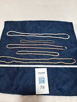 All five pearl necklaces laid flat on fabric with lot card
