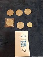 Group photo of six British commemorative coins on dark cloth, one in plastic sleeve