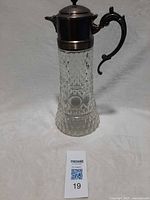 Full view of cut glass pitcher with metal lid and handle