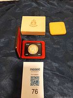 Coin in open clamshell case with outer box and foam pad visible