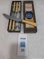 Box open showing five knives in tray with one placed across top; cream handles and stainless blades visible