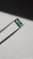 Emerald-cut green tourmaline held in tweezers