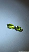 Pair of oval apple-green peridots on neutral background