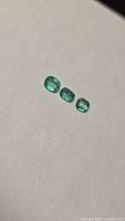 Three loose green cushion-cut emeralds on white background