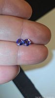 Pair of blue-violet round gemstones on fingertip