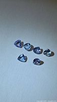 Six loose purple-blue triangular tanzanites on neutral background