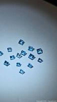 Group of approx. 14 square blue gemstones on white background