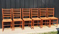 Front view of six orange ladder-back chairs aligned, showing ladder slat backs and rush seats