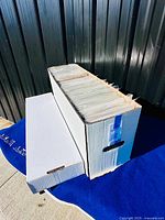 Long white comic long box filled with bagged comics; lid leaning nearby