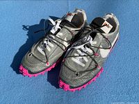 Full view of both sneakers showing upper design and pink spiked outsole